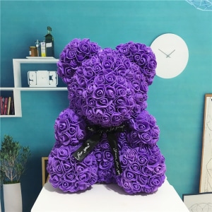 Purple flower bear plush sitting in front of a blue wall with a reloge
