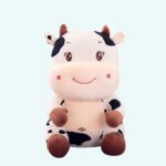 Black and white embroidered baby cow plush on plain background.