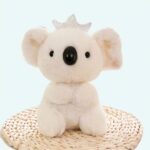 Koala plush with crown sitting on a table with green plant