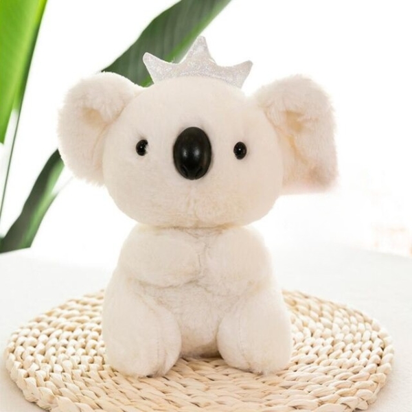 Koala plush with crown sitting on a table with green plant
