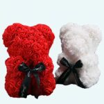 Two teddy bears made of artificial flowers, one is red and the other is white, they are in a black room