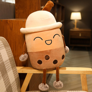 Bubble tea plush laughing with a hat, she is beige and brown, and is sitting on the wooden armrest of a beige, white and brown checked armchair in a flat with a lamp lit in the background