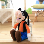 Plush of the goofy character from Disney sitting on a parquet floor, he wears blue trousers and an orange top