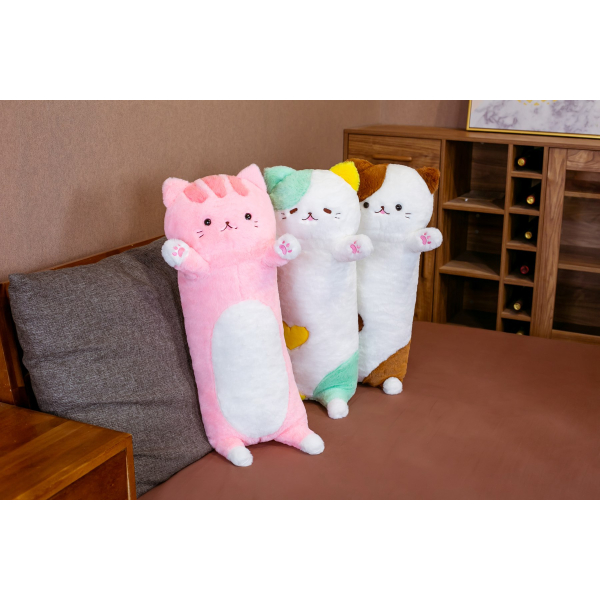 On a grey sofa in a small living room with a brown floor, 3 plush pillows with the effigy of a big cat standing on the sofa, one is pink, the second is green and the third is brown