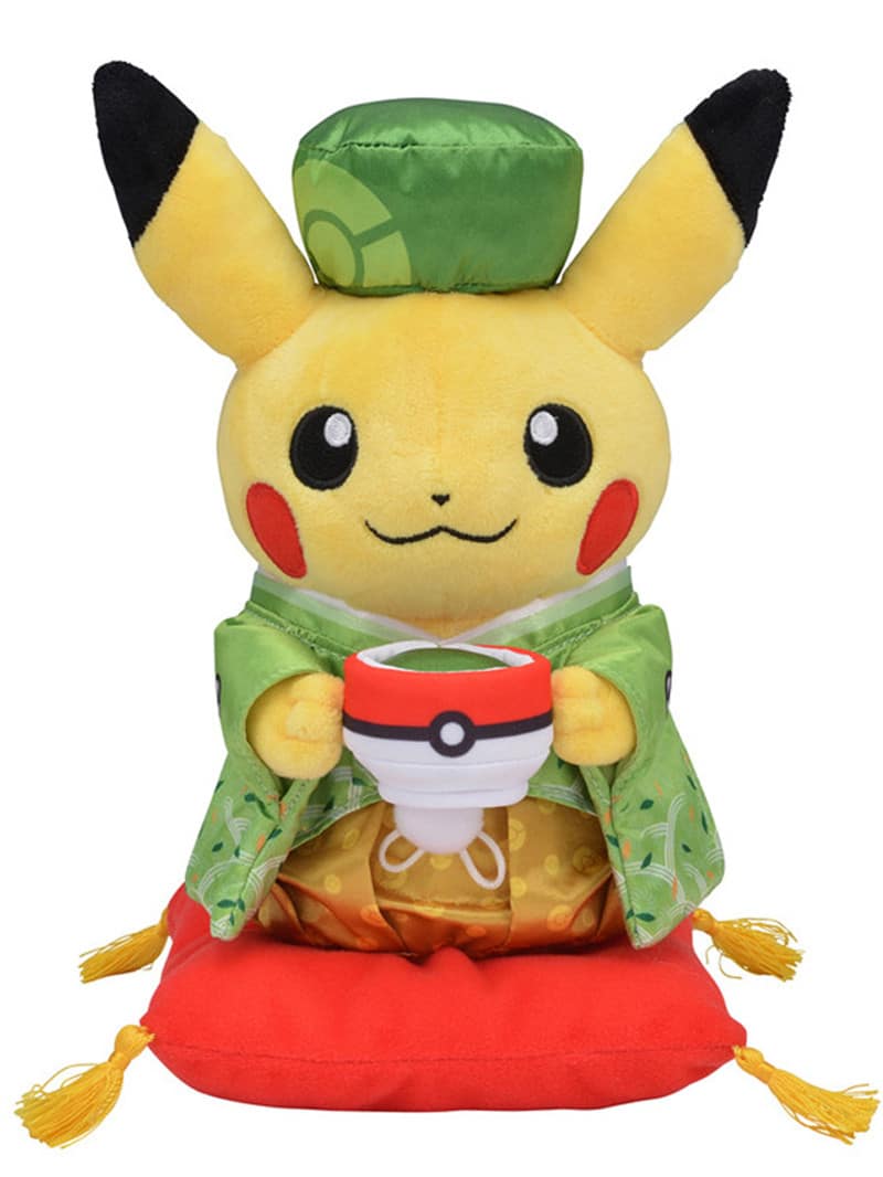 Pikachu plush holding a pokeball and wearing a green Chinese outfit with a matching little hat and standing on a little red cushion