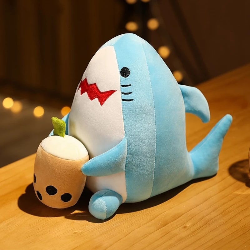 Bubble tea plush in the shape of a blue shark sitting on a wooden table with a small beige pot in his hands