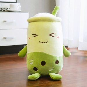 Bubble tea plush in the shape of a green matcha tea which is placed on the floor in front of a white piece of furniture