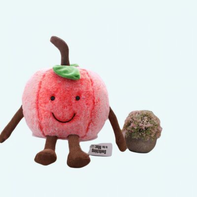 Smiling pink cherry plush on a book and a grey sofa next to a small plant and a coffee table with books in the background