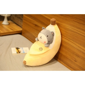 Peeled banana plush with a grey shiba inu inside on a grey bed and a wood coloured wall with a book next to it