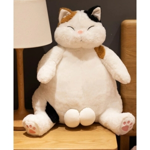 A big white cat with brown and black spots sitting on a wooden table, a white bedside lamp on its right
