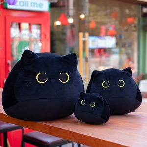Three black plush cats of three different sizes. Placed on a wooden table.