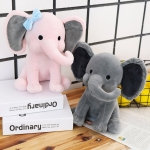 Two elephant cuddly toys, one pink and one grey. The pink one is placed on two white and black books which are placed on a table, the grey one is placed next to it on the wooden table. In the background white tiles