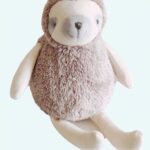A plush sloth sitting on a beige table, with a grey muzzle and grey eyes.