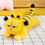 A plush yellow and black striped garfield cat, lying on a black and white checked floor, a pink cushion behind
