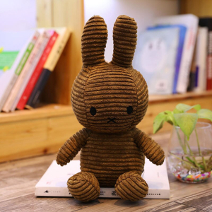 Brown ribbed Miffy plush, on a desk, with a shelf with books in the background