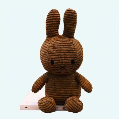 Brown ribbed Miffy plush, on a desk, with a shelf with books in the background