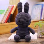 Blue ribbed Miffy plush, on a white book, with a background, a shelf with books