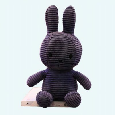 Blue ribbed Miffy plush, on a white book, with a background, a shelf with books