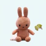 Miffy plush ribbed pink, on a desk, with a background, a shelf with books