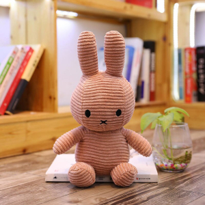 Miffy plush ribbed pink, on a desk, with a background, a shelf with books