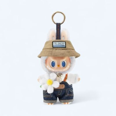 Standing plush with soft cream fur, wearing green overalls with a center pocket, bunny ears, and a mischievous expression, on a neutral background