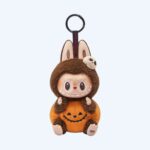 Brown Labubu plush dressed as a pumpkin with a small felt skull on its head and a keychain loop, on a neutral background