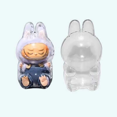 Protective case for seated Labubu-style plush toy, empty on the right and with a blue plush on the left. On light blue background.