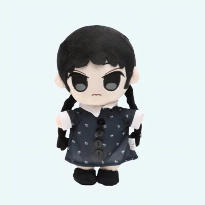 20 cm plush toy of Wednesday Addams with two black braids, a black dress with small white flowers, and a white collar. She has a stern look and a frowning mouth, shown against a light blue background.